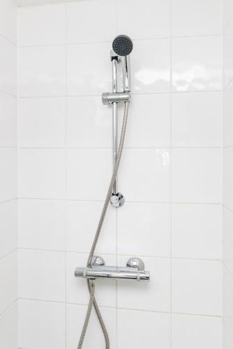 a shower head in a white tiled bathroom at Riverbank Stay in London