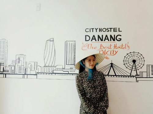 a woman wearing a hat standing in front of a wall at City Hostel Da Nang in Da Nang