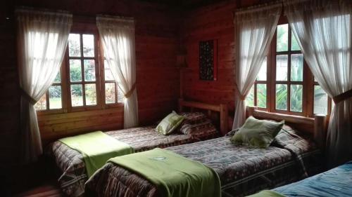 a bedroom with two beds and windows in a cabin at Cabañas Típicas ARIAS in Oxapampa