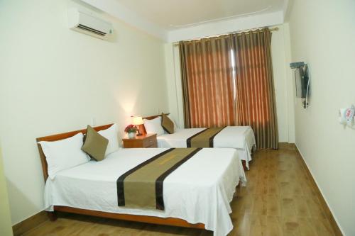 two beds in a hotel room with a window at Gold Plus Hotel in Phong Nha