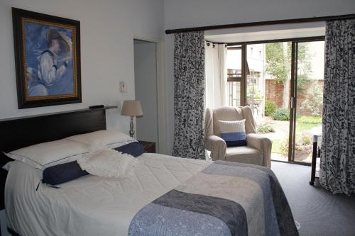 a bedroom with a bed and a chair and a window at Primavera Guest House in Bloemfontein