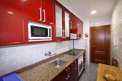 a kitchen with red cabinets and a sink and a microwave at Apartamento con encanto y vistas en playa San Lorenzo in Gijón