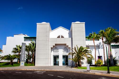 a white building with palm trees in front of it at Barceló Teguise Beach - Adults Only in Costa Teguise