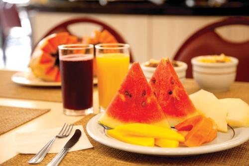 a plate of fruit on a table with two glasses of juice at Lira Hotel in Curitiba