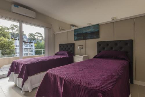 2 camas en una habitación con sábanas moradas y una ventana en Boreas Carilo en Cariló