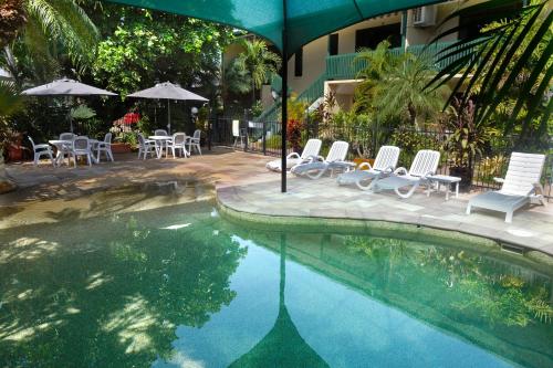 a swimming pool with chairs and tables and an umbrella at City Gardens Apartments in Darwin