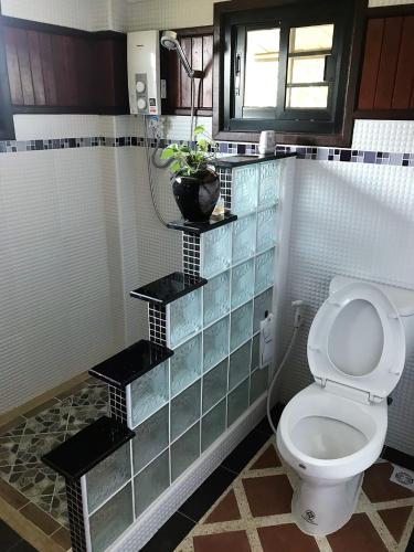 a bathroom with a toilet with three shelves at Tum Baan Suan ตุ่มบ้านสวน in Chanthaburi