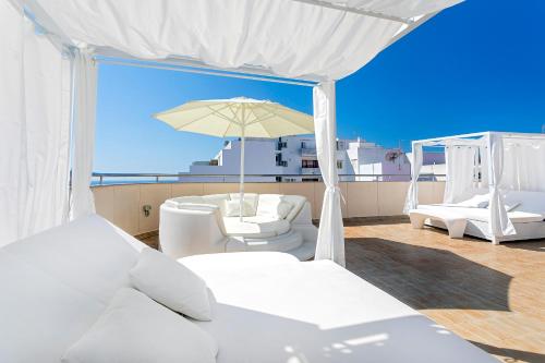 einen Balkon mit weißen Möbeln und einem Sonnenschirm in der Unterkunft Aparthotel Duquesa Playa in Santa Eulària des Riu