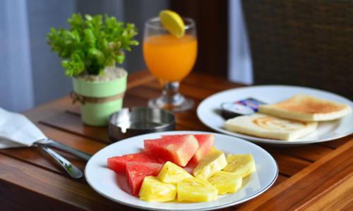stół z dwoma talerzami owoców i szklanką soku pomarańczowego w obiekcie Puri Kesari Guest House w mieście Sanur