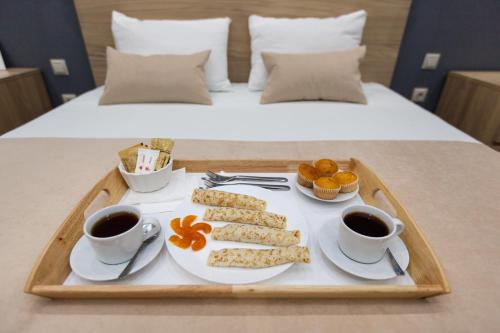 モスクワにあるMini Hotel Brusnika na Amurskayaのベッドの上にコーヒー2杯と食料品のトレイ