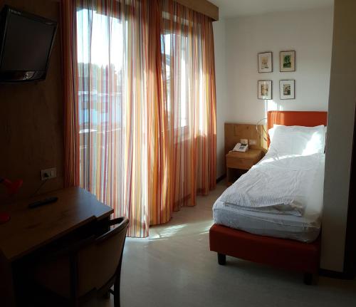 a bedroom with a bed and a desk and a window at Hotel Olimpic in Baselga di Pinè