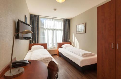 a hotel room with two beds and a desk and a window at A-Train Hotel in Amsterdam