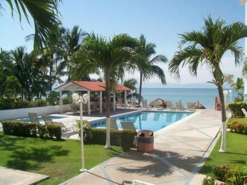 a swimming pool with palm trees and the ocean at Hotel y Suites Corita in Bucerías