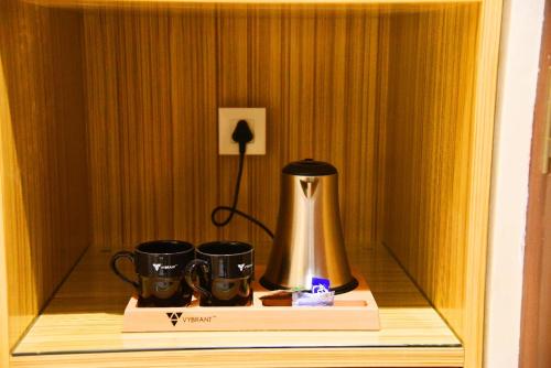 una cafetera y dos tazas en un estante en Mango Hotels Vijayawada en Vijayawāda
