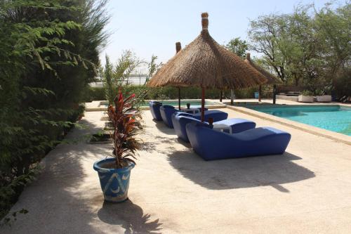a row of blue chairs and an umbrella next to a pool at Hôtel Les Cordons Bleus in Ndangane