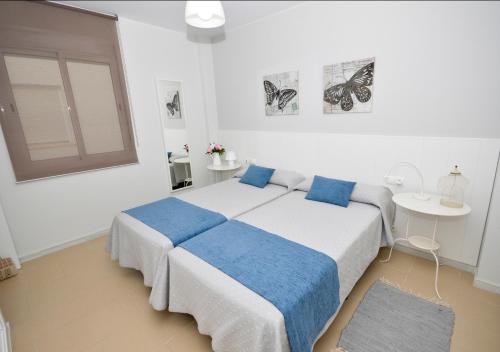 a white bedroom with two beds with blue pillows at Apartamento Mariposa in Conil de la Frontera