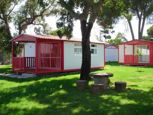 a red and white cabin with a tree in the grass at Parque de Campismo Orbitur Montargil in Montargil