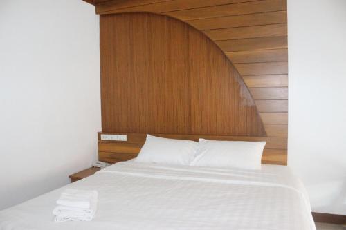 a bed with a wooden headboard and white sheets at Tree Home Plus in Nakhon Si Thammarat