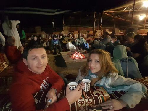 a man and woman holding coffee cups in front of a fire at Wadi Rum Dream Camp in Wadi Rum