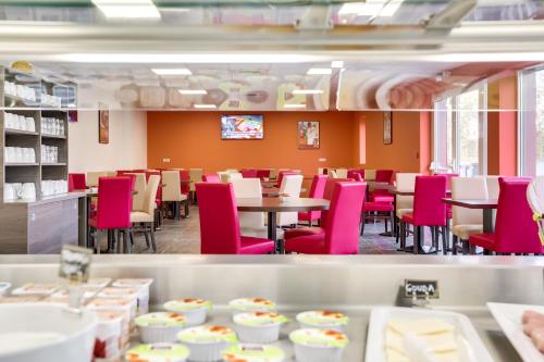 a dining room with pink chairs and tables at The Originals City, Hôtel Caen Mémorial in Caen