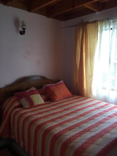a bedroom with a bed with a striped blanket and a window at Cabañas Las Palmeras Pichilemu in Pichilemu