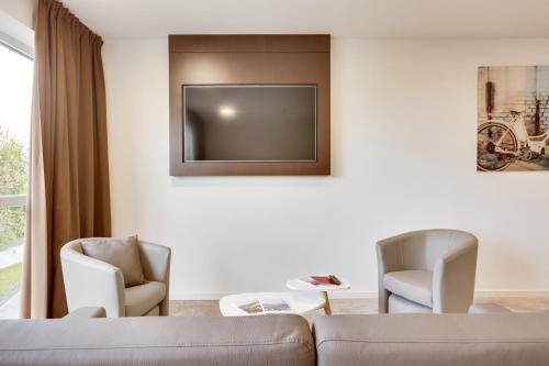 a living room with a couch and two chairs and a tv at The Originals City, Hôtel Caen Mémorial in Caen
