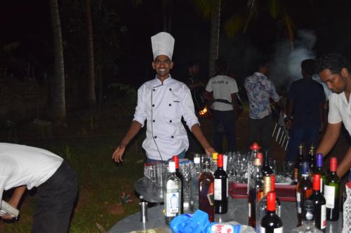 a chef standing next to a table with bottles of wine at The Coconut Gardens Hotel & Restaurant in Tissamaharama
