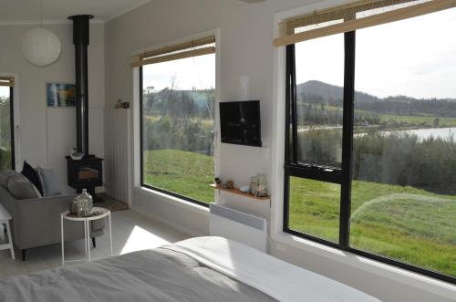 a bedroom with large windows and a bed and a tv at Flotsam Studio Dunalley in Dunalley