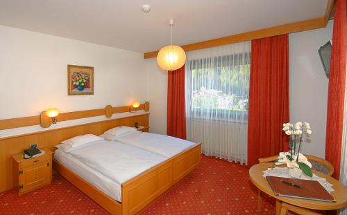 Schlafzimmer mit einem Bett, einem Tisch und einem Fenster in der Unterkunft Garni Hotel Rezia in Wolkenstein in Gröden