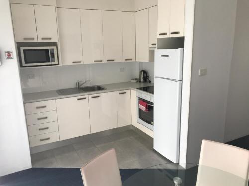 a kitchen with white cabinets and a white refrigerator at Aquarius Apartments Mollymook in Mollymook
