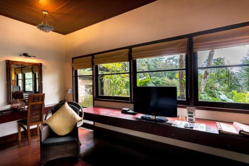 a living room with a desk with a tv and windows at Bidadari Private Villas & Retreat in Ubud