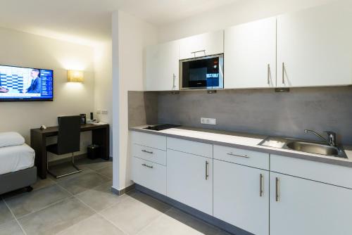 a kitchen with white cabinets and a sink and a desk at DuDa Boarding Apartments in Langenbruck
