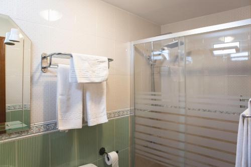 y baño con cabina de ducha de cristal y toallas. en Pensión y apartamentos El Taxi, en Casabermeja