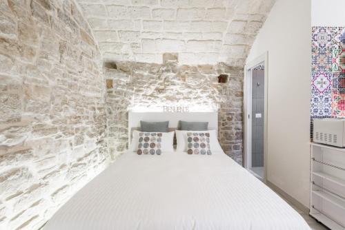 sypialnia z białym łóżkiem i kamienną ścianą w obiekcie San Nicola Old Town Apartment Casatuabari w mieście Bari