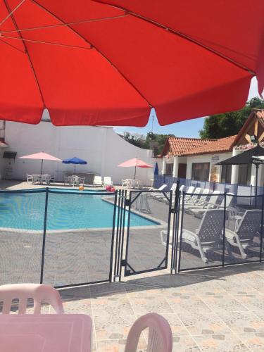 a pool with a red umbrella and chairs and a swimming pool at Hotel Villa Ricaurte in Girardot