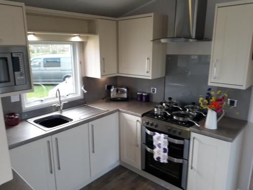a kitchen with white cabinets and a stove and a sink at Aspen Retreat, Haggerston Castle in Cheswick