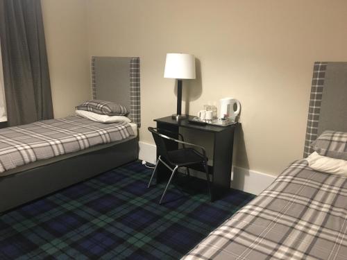 a room with two beds and a desk and a chair at Crookston Hotel in Glasgow