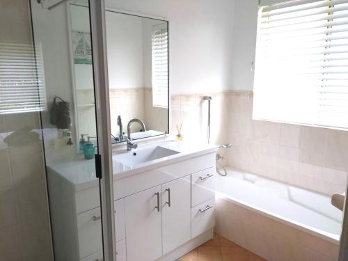 a bathroom with a sink and a tub and a mirror at Fairway Haven Getaway in Mollymook