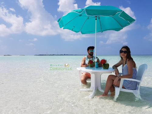 a man and woman sitting at a table under an umbrella on the beach at Rasdhoo Coralville in Rasdu