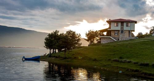 a house on the shore of a lake with a boat at Divna Guest House in Dospat