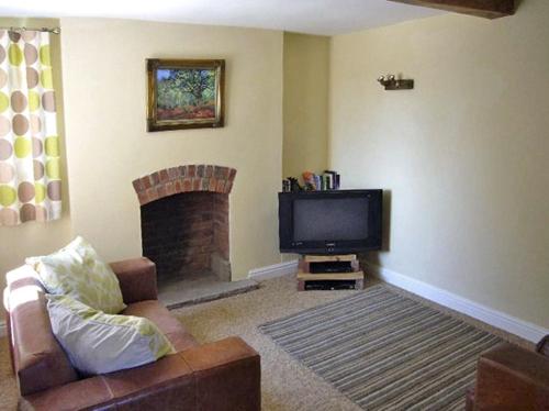 a living room with a couch and a tv and a fireplace at Manor Cottage in Ludlow