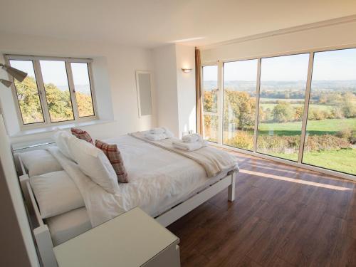 a white bedroom with a bed and large windows at Beautiful Cotswold View in Bourton on the Water