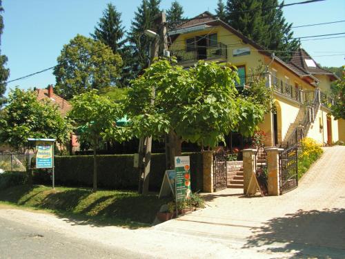 a house with a tree on the side of a street at Nefelejcs Fagyizó és Apartmanház in Kistolmács