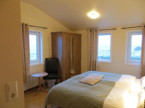 a bedroom with a bed and a chair and two windows at Guesthouse Vellir in Vík