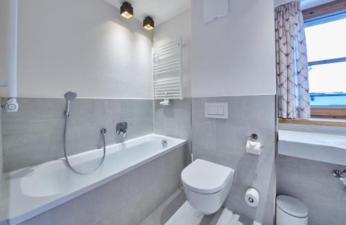 a white bathroom with a toilet and a bath tub at Chalet Guter Hirte in Saalbach Hinterglemm
