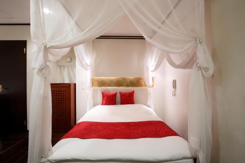 1 dormitorio con cama blanca con dosel y almohadas rojas en Hotel The Lotus Bali (Adult Only), en Kawasaki