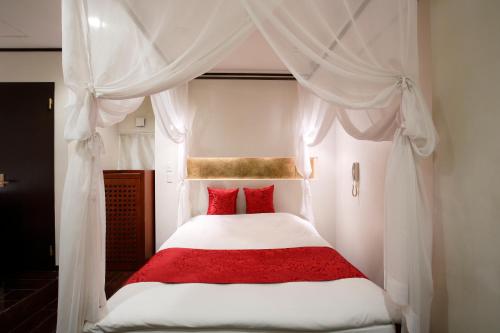 a bedroom with a white canopy bed with red pillows at Hotel The Lotus Bali (Adult Only) in Kawasaki
