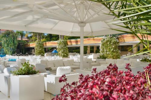 a white patio with white chairs and an umbrella at Hotel Ariston in Paestum