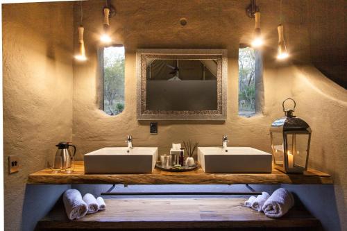 a bathroom with two sinks and a mirror and lights at Garonga Safari Camp in Makalali Game Reserve