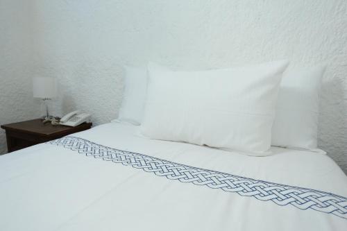 a bed with white sheets and a phone on a table at Hotel Casa Colonial Boutique in Managua